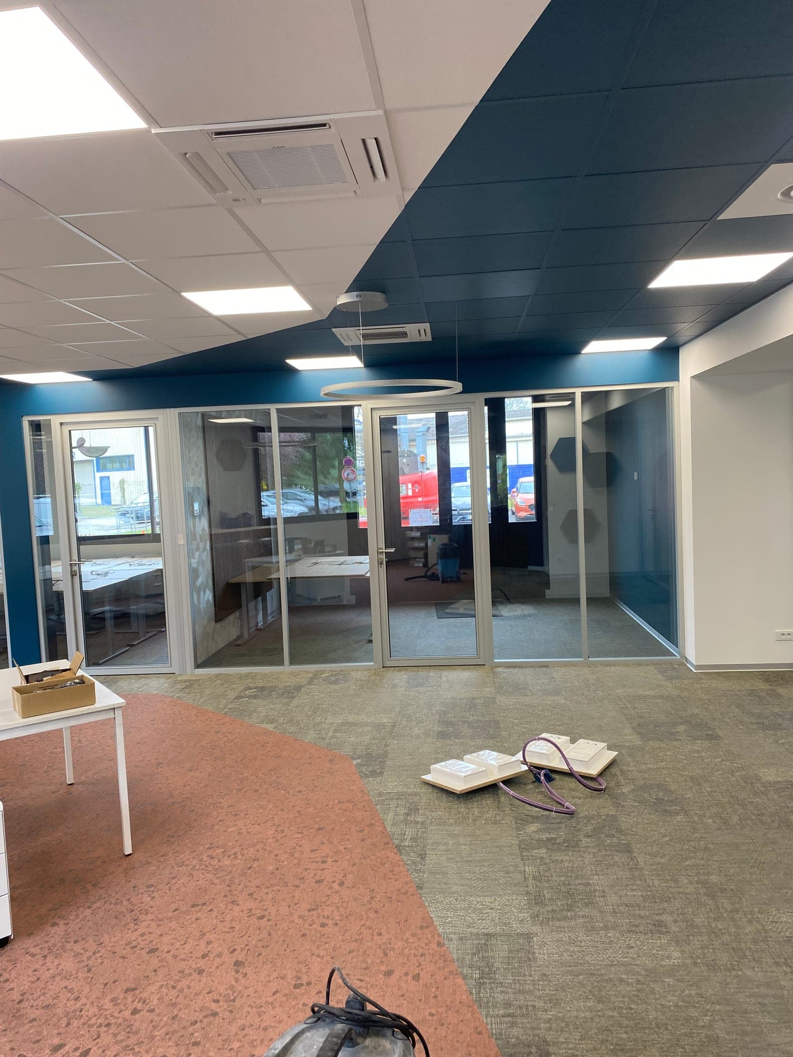 Vue d'ensemble du showroom fini — vitrines verre, mur bleu canard, sol moquette grise
